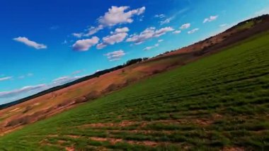 Dikey video FPV dron görüntüsü canlı yeşil alanlar üzerinde bankacılık ve dağınık bulutlar altında açık mavi gökyüzü altında yuvarlanan kırsal. Manzaralı kırsal alan, hızlı hareket, dinamik hava fpv dronu