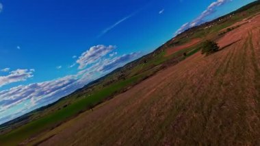 Dikey video FPV dron görüntüsü canlı yeşil alanlar üzerinde bankacılık ve dağınık bulutlar altında açık mavi gökyüzü altında yuvarlanan kırsal. Manzaralı kırsal alan, hızlı hareket, dinamik hava fpv dronu