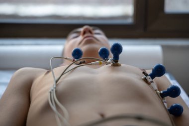 Kadın bir doktor, hastane odasında genç bir adama EKG çeker. Rutin bir kontrol sırasında kalp sağlığını dikkatle izler.