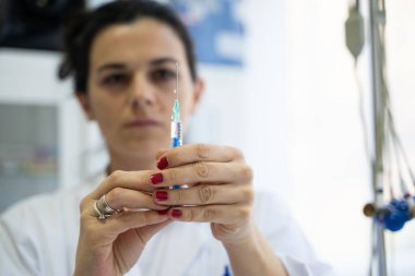 Beyaz önlüklü, odaklanmış bir hemşire profesyonel bir sağlık ortamında enjeksiyon için dikkatlice bir şırınga hazırlar.