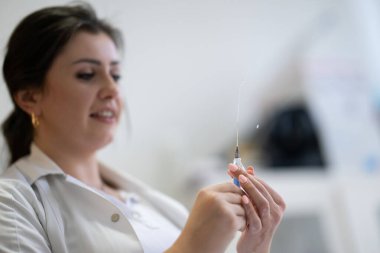 Beyaz önlüklü, odaklanmış bir hemşire profesyonel bir sağlık ortamında enjeksiyon için dikkatlice bir şırınga hazırlar.