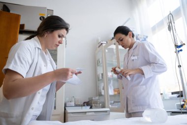 Bir hastane laboratuvarında iki hemşire hastalar ve hastane kullanımı için ilaçları dikkatlice inceliyor ve hazırlıyorlar.