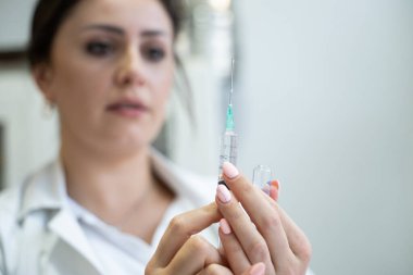 Beyaz önlüklü, odaklanmış bir hemşire profesyonel bir sağlık ortamında enjeksiyon için dikkatlice bir şırınga hazırlar.