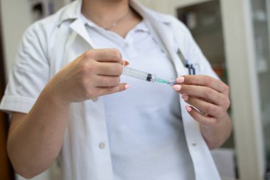 Beyaz önlüklü, odaklanmış bir hemşire profesyonel bir sağlık ortamında enjeksiyon için dikkatlice bir şırınga hazırlar.