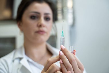 Beyaz önlüklü, odaklanmış bir hemşire profesyonel bir sağlık ortamında enjeksiyon için dikkatlice bir şırınga hazırlar.