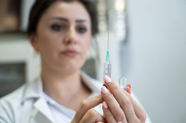 Beyaz önlüklü, odaklanmış bir hemşire profesyonel bir sağlık ortamında enjeksiyon için dikkatlice bir şırınga hazırlar.