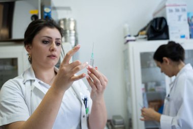 Beyaz önlüklü, odaklanmış bir hemşire profesyonel bir sağlık ortamında enjeksiyon için dikkatlice bir şırınga hazırlar.