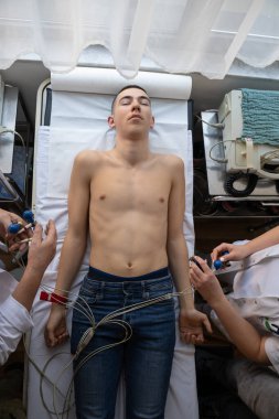 Kadın bir doktor, hastane odasında genç bir adama EKG çeker. Rutin bir kontrol sırasında kalp sağlığını dikkatle izler.