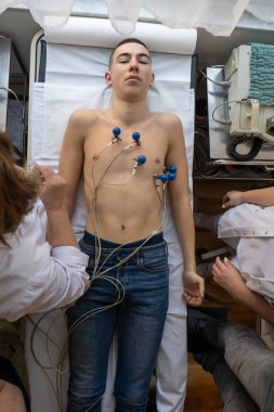 Kadın bir doktor, hastane odasında genç bir adama EKG çeker. Rutin bir kontrol sırasında kalp sağlığını dikkatle izler.