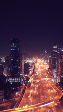 İkonik gökdelenlerin gece görüşü ve Dubai, BAE 'deki büyük bir kavşakta yoğun trafik. Modern bir şehrin çarpıcı silueti iş, finans ve kentsel gelişimi sembolize ediyor..