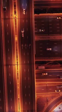 Parlayan gece trafiğinin, akıllı Dubai şehrindeki fütüristik gökdelenlerle çevrili otoyol kavşaklarından dokumasının en üst görüntüsü. Canlı şehir ışıkları, modern ufuk çizgisi ve şehir mimarisi.