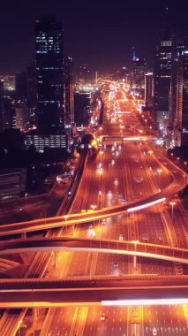 Parlayan gece trafiğinin, akıllı Dubai şehrindeki fütüristik gökdelenlerle çevrili otoyol kavşaklarından dokumasının en üst görüntüsü. Canlı şehir ışıkları, modern ufuk çizgisi ve şehir mimarisi.