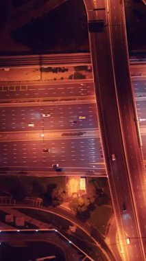 Parlayan gece trafiğinin, akıllı Dubai şehrindeki fütüristik gökdelenlerle çevrili otoyol kavşaklarından dokumasının en üst görüntüsü. Canlı şehir ışıkları, modern ufuk çizgisi ve şehir mimarisi.