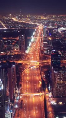 İkonik gökdelenlerin gece görüşü ve Dubai, BAE 'deki büyük bir kavşakta yoğun trafik. Modern bir şehrin çarpıcı silueti iş, finans ve kentsel gelişimi sembolize ediyor..