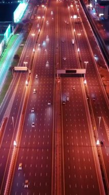 Parlayan gece trafiğinin, akıllı Dubai şehrindeki fütüristik gökdelenlerle çevrili otoyol kavşaklarından dokumasının en üst görüntüsü. Canlı şehir ışıkları, modern ufuk çizgisi ve şehir mimarisi.
