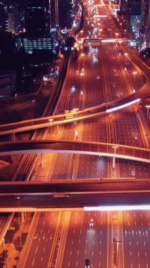 Parlayan gece trafiğinin, akıllı Dubai şehrindeki fütüristik gökdelenlerle çevrili otoyol kavşaklarından dokumasının en üst görüntüsü. Canlı şehir ışıkları, modern ufuk çizgisi ve şehir mimarisi.