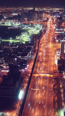 Parlayan gece trafiğinin, akıllı Dubai şehrindeki fütüristik gökdelenlerle çevrili otoyol kavşaklarından dokumasının en üst görüntüsü. Canlı şehir ışıkları, modern ufuk çizgisi ve şehir mimarisi.
