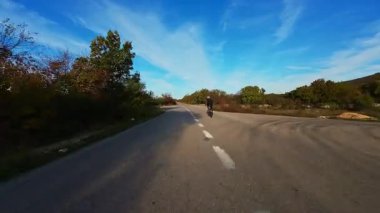 Gün batımında virajlı dağ yolunda bisikletçi. Etrafı canlı sonbahar yapraklarıyla çevrili. Seyahat macerası için ideal doğa ve mevsimsel yaşam tarzı temaları.