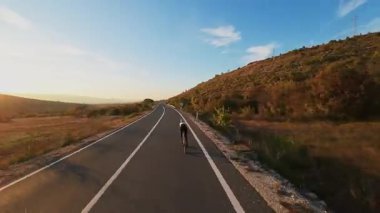 Gün batımında virajlı dağ yolunda bisikletçi. Etrafı canlı sonbahar yapraklarıyla çevrili. Seyahat macerası için ideal doğa ve mevsimsel yaşam tarzı temaları.