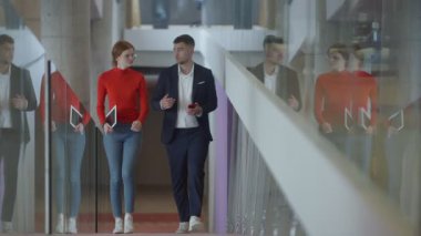 Modern bir girişim şirketinin dinamik ortamında, yönetici genç iş arkadaşı ile yürürken bir tartışma içine girer, işbirliği ve yenilik ruhunu yansıtır.