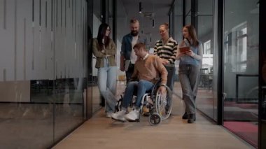 Tekerlekli sandalyede engelli bir iş adamı, modern bir ofiste takım çalışmasının, dahil olmanın ve güçlenmenin gücünü ortaya koyan destekleyici meslektaşlarıyla çevrilidir.. 