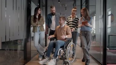 Tekerlekli sandalyede engelli bir iş adamı, modern bir ofiste takım çalışmasının, dahil olmanın ve güçlenmenin gücünü ortaya koyan destekleyici meslektaşlarıyla çevrilidir.. 