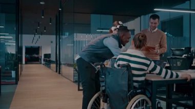 Modern bir iş yerinde çalışan tekerlekli sandalyedeki engelli bir iş kadını. Çevredeki ekip sanal gerçeklik gözlükleri kullanıyor, açık alan yaratıcılığında en son teknolojiyle işbirliği yapıyorlar.