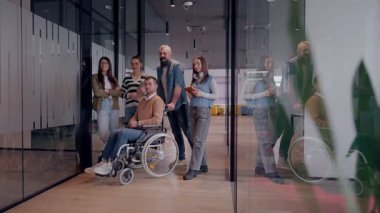 Tekerlekli sandalyede engelli bir iş adamı, modern bir ofiste takım çalışmasının, dahil olmanın ve güçlenmenin gücünü ortaya koyan destekleyici meslektaşlarıyla çevrilidir.. 
