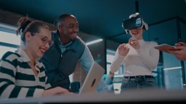 Modern bir iş yerinde çalışan tekerlekli sandalyedeki engelli bir iş kadını. Çevredeki ekip sanal gerçeklik gözlükleri kullanıyor, açık alan yaratıcılığında en son teknolojiyle işbirliği yapıyorlar.