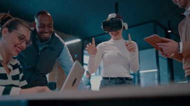 Modern bir iş yerinde çalışan tekerlekli sandalyedeki engelli bir iş kadını. Çevredeki ekip sanal gerçeklik gözlükleri kullanıyor, açık alan yaratıcılığında en son teknolojiyle işbirliği yapıyorlar.