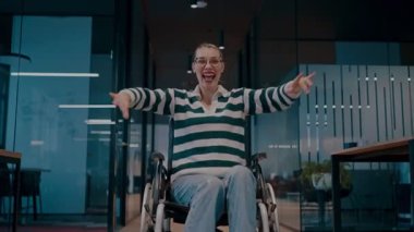 Tekerlekli sandalyede engelli neşeli bir kadın modern bir ofis, kapsamlı bir iş yeri, güç, başarı, erişilebilirlik ve dinamik bir pozitiflikte kollarını kaldırıyor.