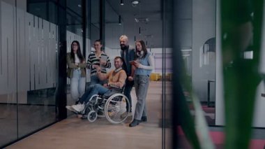 Tekerlekli sandalyede engelli bir iş adamı, modern bir ofiste takım çalışmasının, dahil olmanın ve güçlenmenin gücünü ortaya koyan destekleyici meslektaşlarıyla çevrilidir.. 