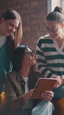 Kadın iş adamları pencere kenarında iş birliği yapıyor, fikirleri tartışıyor ve tablet üzerinde beyin fırtınası yapıyorlar. Modern bir ofiste işbirliği, yaratıcılık ve takım çalışması kavramı