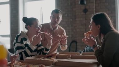 Modern bir ofis alanında pizzadan keyif alan çeşitli genç profesyonellerden oluşan bir grup, rahat ve işbirlikçi bir atmosfer yaratıyorlar. Takım çalışması temaları, sıradan toplantılar ve işyeri için mükemmel.