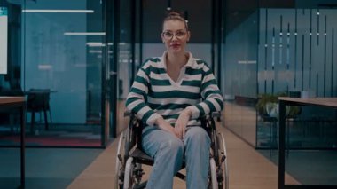 Tekerlekli sandalyede engelli neşeli bir kadın modern bir ofis, kapsamlı bir iş yeri, güç, başarı, erişilebilirlik ve dinamik bir pozitiflikte kollarını kaldırıyor.