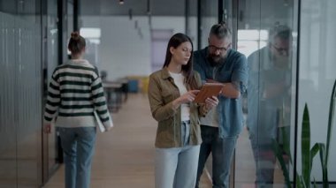 Üst düzey bir hipster akıl hocası ve Avrupalı bir lider, modern bir çalışma alanında tablet üzerinde çalışırken, arka planda yoğun meslektaşlar çalışırken güvenli bir şekilde işbirliği yaparak bir projeyi tartışıyorlar.