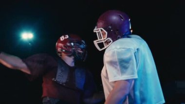 İki Amerikan futbolcusunun karşılaşması, kaskların parlak stadyum ışıkları altında çarpışması, takım rekabetini, kararlılığını ve iş dünyasındaki rekabet ruhunu sembolize eden dramatik bir an.