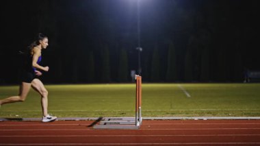 Dişi sporcu bir engele doğru koşuyor, engelli koşuyor, yüksek hızda bariyerin üzerinden atlıyor bir yarışta koşarken. Hız Rampası Efektli Süper Yavaş Sinema Görüntüsü.