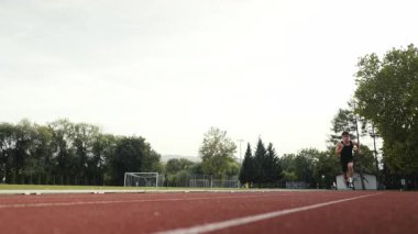Güneşli bir sabahta atletizm pistinde koşan genç bir sporcunun dikey videosu. Spor anlayışı ve azim. Yüksek kalite 4k görüntü