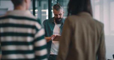 Sakallı kıdemli çok ırklı iş adamı gülümseyip kameraya bakıyor. Olgun CEO, modern bir açık mekan ortaklaşa çalışma ofisinde dijital tablet tutuyor ve akıllı, gelişigüzel liderlik gösteriyor.