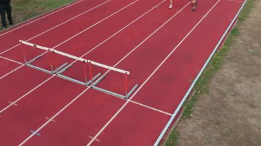 Bir stadyum pistinde yan yana koşan atletik bir çiftin yukarıdan gelen hava aracı atışı, yavaş çekimde, mükemmel bir senkronizasyon içinde hareket ederlerken zindeliklerini, ritmlerini ve enerjilerini vurguluyor.