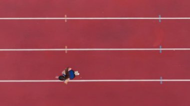 Büyük bir stadyum atletizm pistinde koşan profesyonel bir bayan sporcunun havadan drone görüntüsü. Dinamik yavaş çekim sinematik görüntüler onun gücünü, hızını ve kararlılığını yakalar.