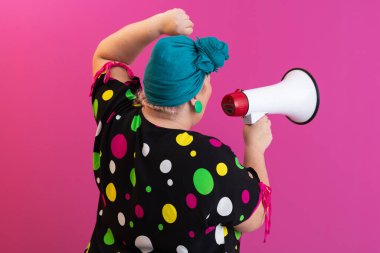 Renkli puantiyeli kıyafetli kendine güvenen bir kadın ve eski kafa örtüsü ile megafona bağırıyor, güçlü bir duygu ve tavır sergiliyor.. 