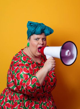 Renkli puantiyeli kıyafetli kendine güvenen bir kadın ve sarı bir arka plana karşı güçlü duygu ve tutumunu ifade eden megafona bağıran retro başlıklı bir kadın.. 