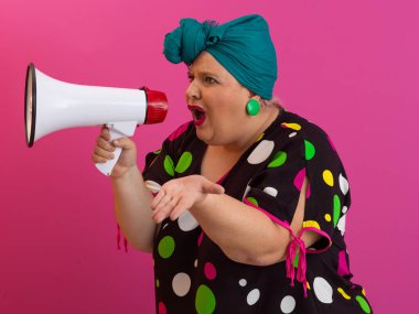 Renkli puantiyeli kıyafetli kendine güvenen bir kadın ve eski kafa örtüsü ile megafona bağırıyor, güçlü bir duygu ve tavır sergiliyor.. 