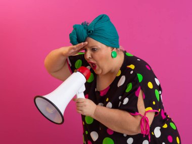 Renkli puantiyeli kıyafetli kendine güvenen bir kadın ve eski kafa örtüsü ile megafona bağırıyor, güçlü bir duygu ve tavır sergiliyor.. 