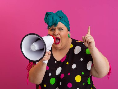 Renkli puantiyeli kıyafetli kendine güvenen bir kadın ve eski kafa örtüsü ile megafona bağırıyor, güçlü bir duygu ve tavır sergiliyor.. 