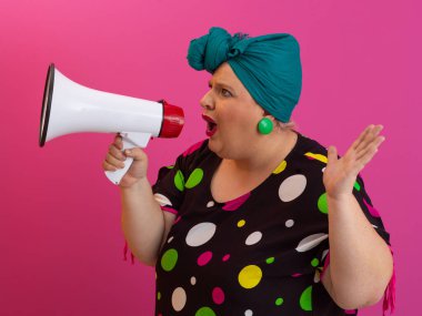 Renkli puantiyeli kıyafetli kendine güvenen bir kadın ve eski kafa örtüsü ile megafona bağırıyor, güçlü bir duygu ve tavır sergiliyor.. 