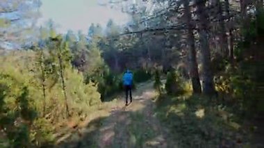 Ağaçlar ve güneş ışığıyla çevrili, manzaralı bir orman yolunda koşan bir adamın FPV görüntüsü. Açık hava fitness, sağlıklı yaşam tarzı, ve dayanıklılık ve motivasyon için atletik eğitim