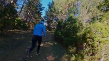 Ağaçlar ve güneş ışığıyla çevrili, manzaralı bir orman yolunda koşan bir adamın FPV görüntüsü. Açık hava fitness, sağlıklı yaşam tarzı, ve dayanıklılık ve motivasyon için atletik eğitim